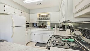Una cocina moderna con muebles blancos, estufa de acero inoxidable y encimera de mármol.