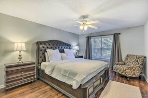 A bedroom with a tufted headboard bed, a nightstand with a lamp, a patterned armchair, and a window with curtains. - Auburn Home w/ Private Yard < 4 Mi to Campus! (Auburn)
