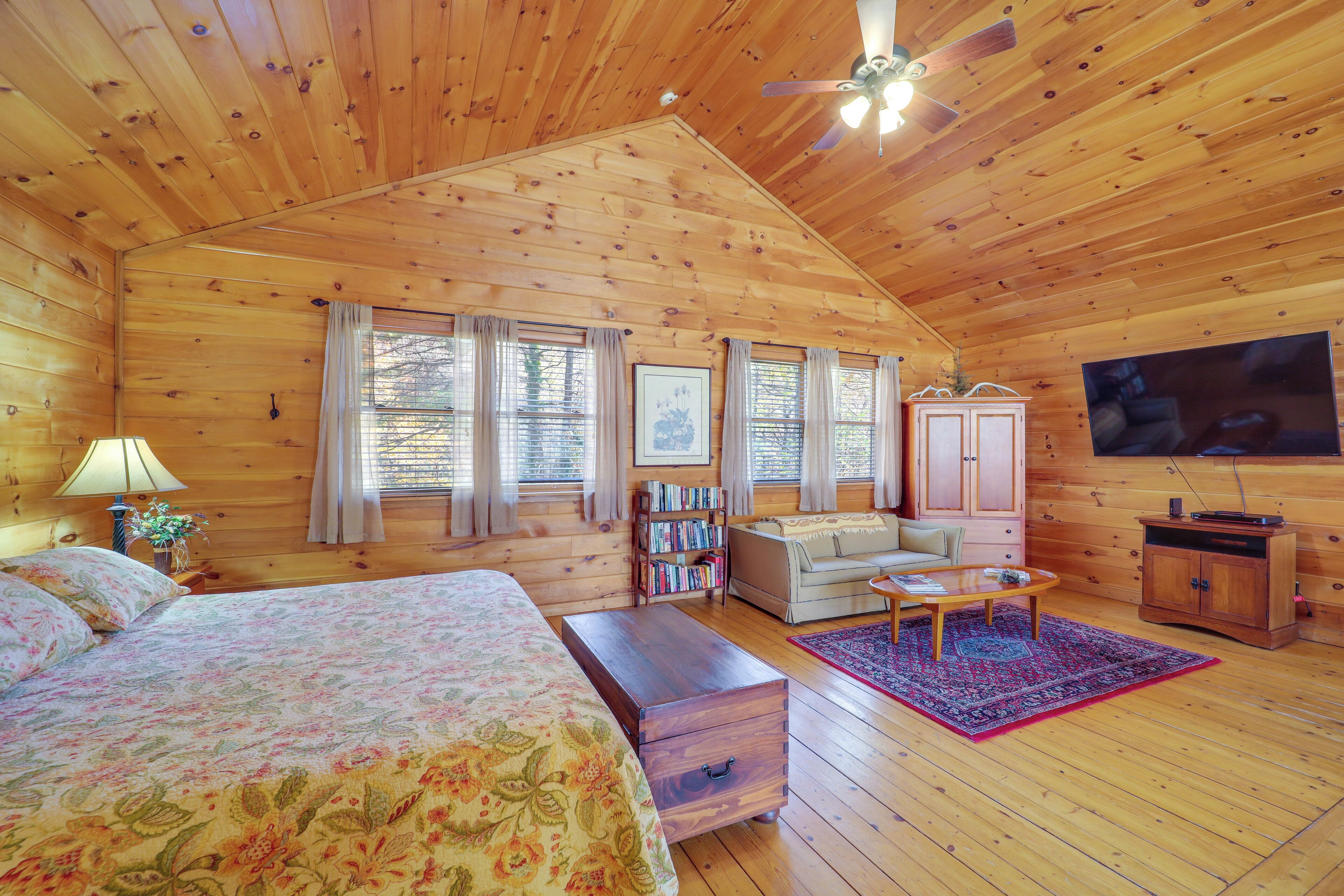 A cozy log cabin bedroom with a bed, a wooden chest, a sofa, a coffee table, and a television.