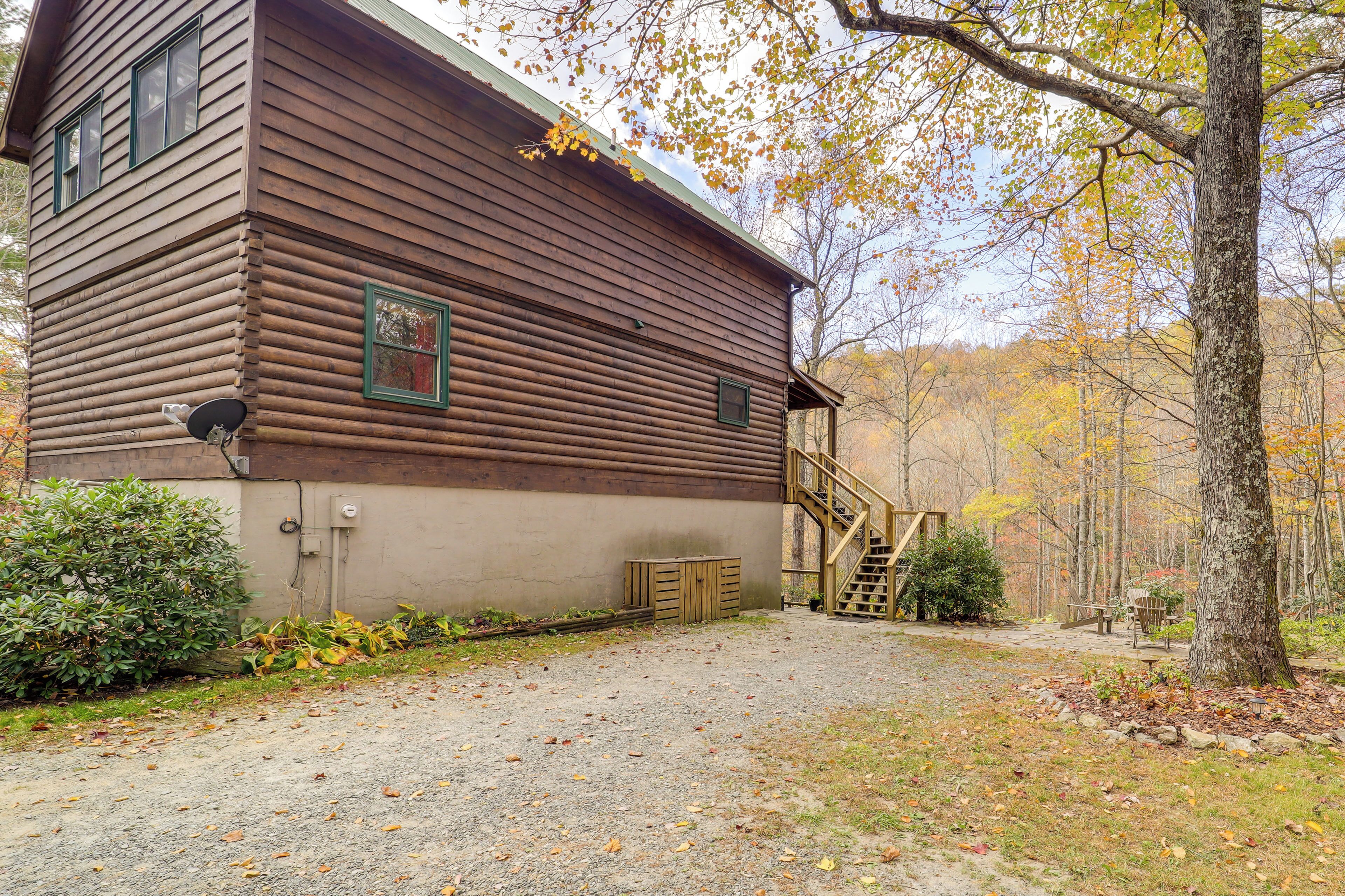 A rustic log cabin with a gravel driveway, a wooden staircase, and a small porch area.