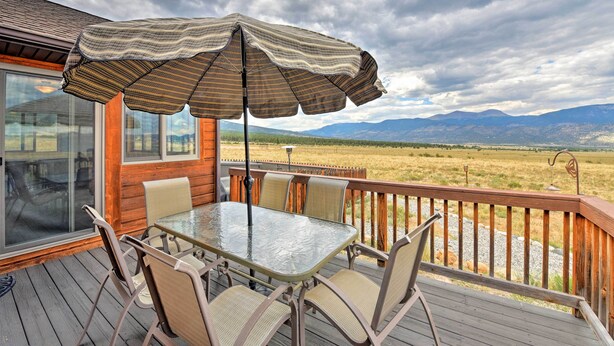 A deck with a glass table and chairs, an umbrella, and a view of a field and mountains. - Buena Vista Retreat: 7 Acres & Panoramic Views (Buena Vista)