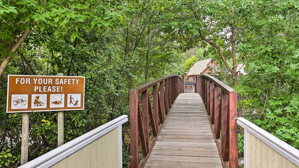 A wooden pedestrian bridge with safety signs and a metal railing. - Central Creekfront Spearfish Apt by City Park (Spearfish)