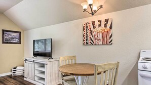 A dining area with a wooden table and chairs, a white cabinet with a television, and a popcorn-themed artwork on the wall. - Central Creekfront Spearfish Apt by City Park (Spearfish)