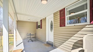 A covered porch with a table and chairs, a door, and a window with shutters.