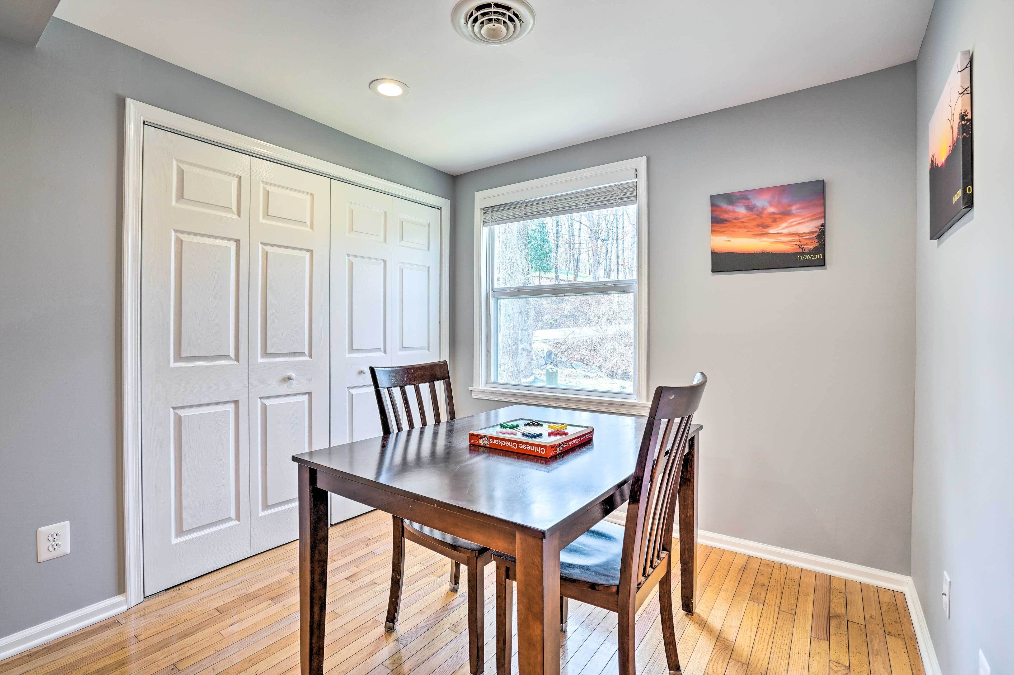 Un coin repas avec une table et des chaises en bois, une fenêtre avec des stores, une porte et un tableau encadré au mur.
