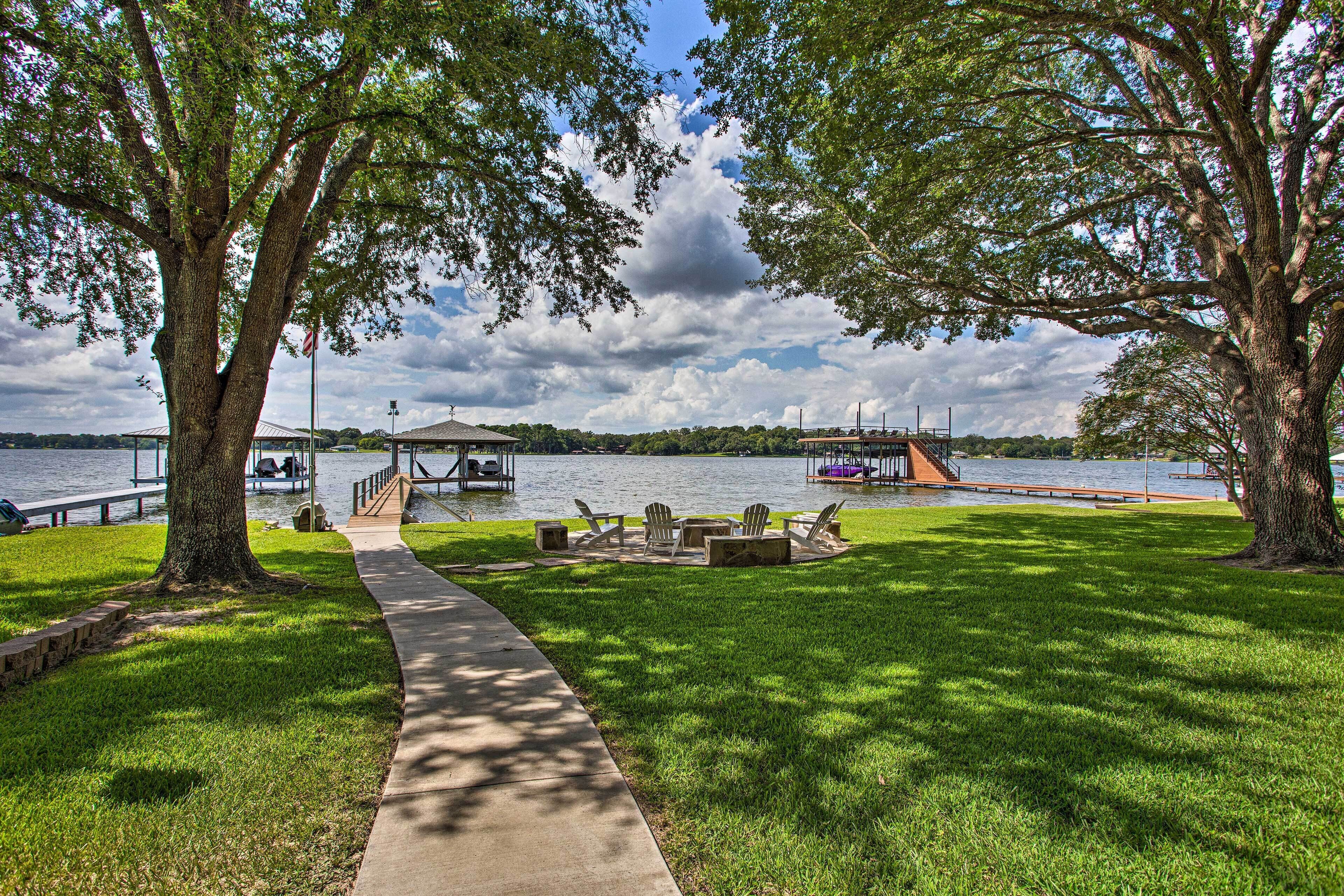 A park with a concrete path, picnic tables, and a dock by a lake.