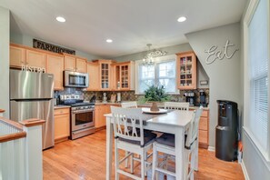 Une cuisine dotée de meubles en bois, d’appareils électroménagers en acier inoxydable, d’un coin repas avec des chaises blanches et d’un distributeur d’eau.