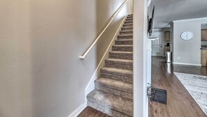A carpeted staircase with a handrail, leading to a room with wooden flooring and a white wall clock. - Charming Springdale Townhome ~ 5 Mi to Dtwn! (Springdale)
