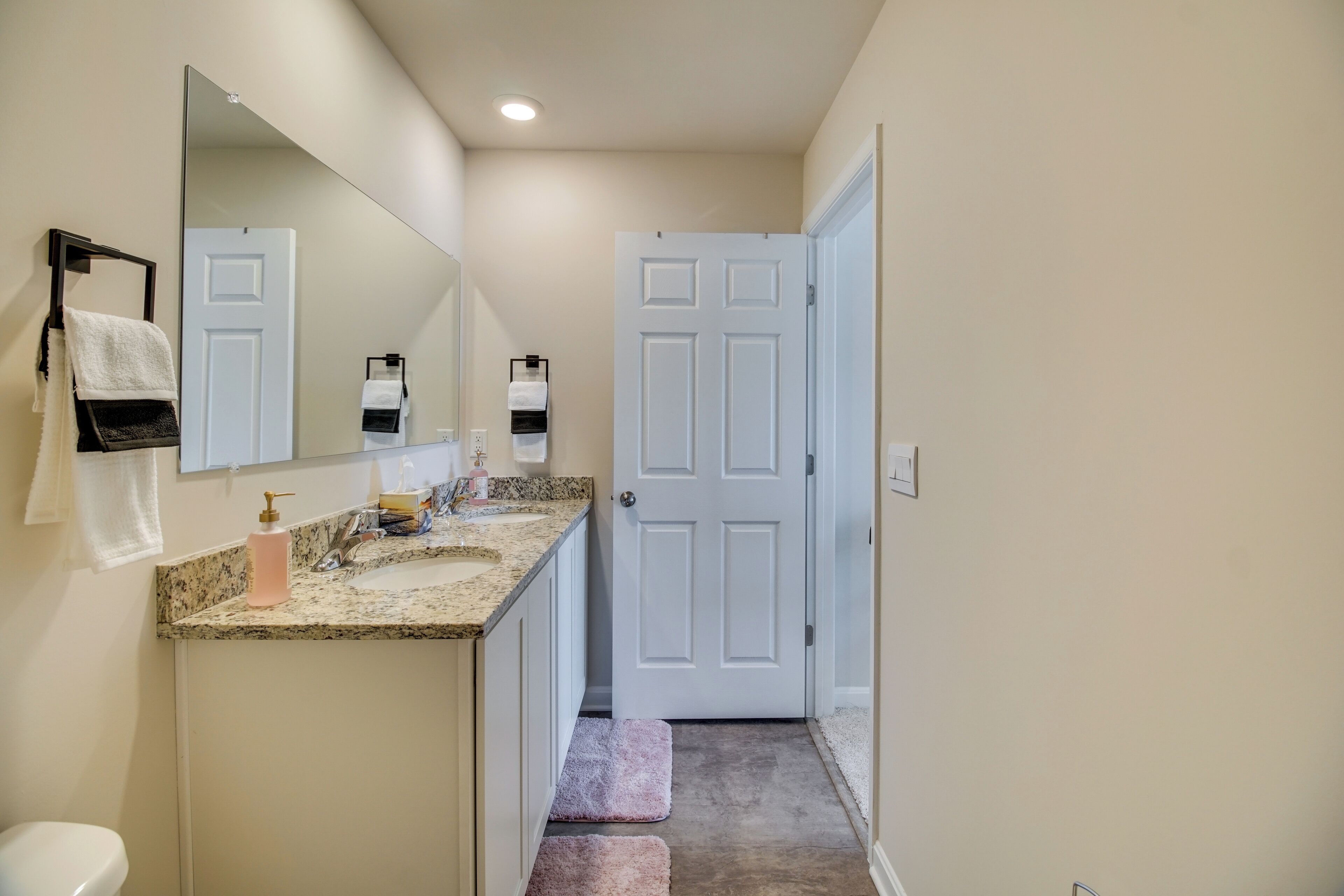 Une salle de bain avec des toilettes blanches, un lavabo doté d’un plan de travail en granit, un miroir et une porte blanche.
