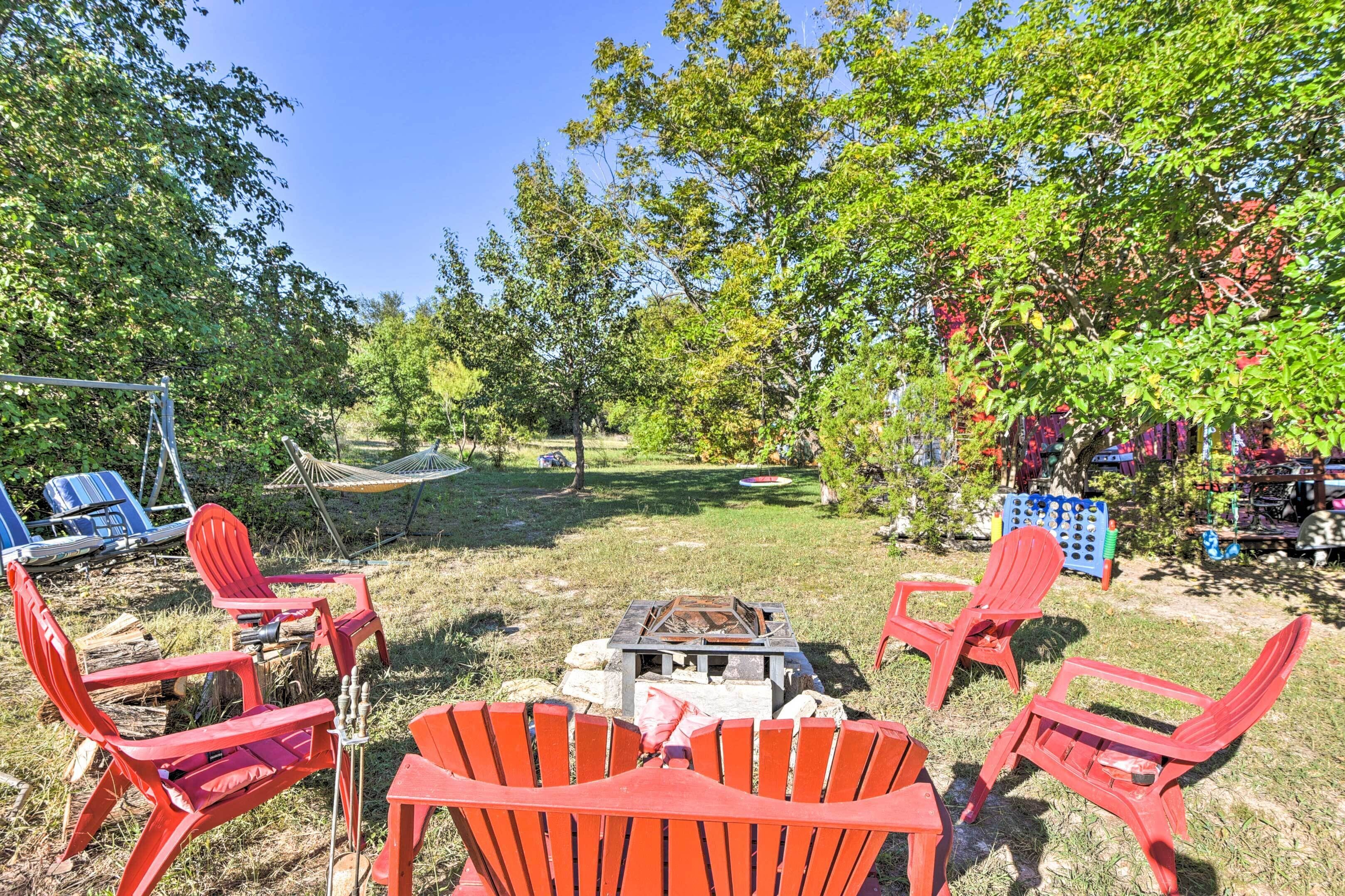 Un jardin avec des chaises rouges, un foyer et un hamac.