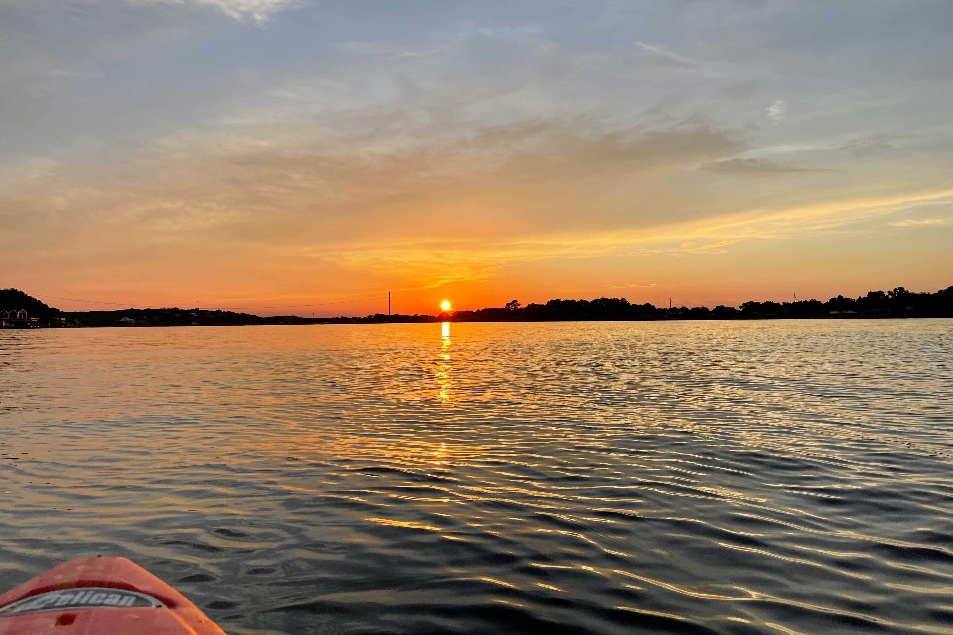 A sunset over a calm body of water with a distant shoreline.