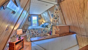 Een gezellig slaapkamer op zolder met schuine wanden, een bed met beddengoed met een patroon, een houten bureau en een raam met uitzicht.
