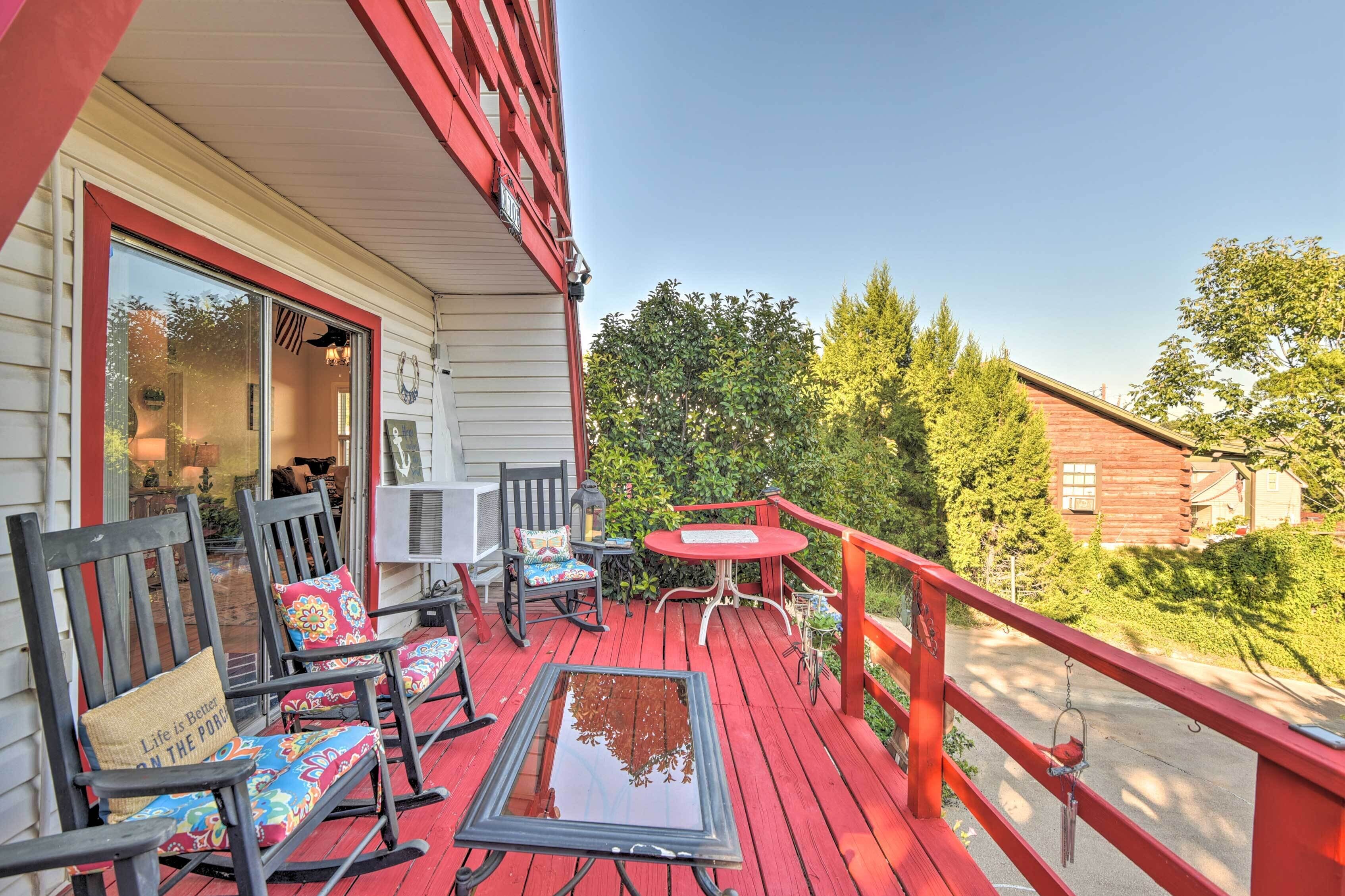 A wooden deck with red railings, outdoor seating, and a view of a forested area.