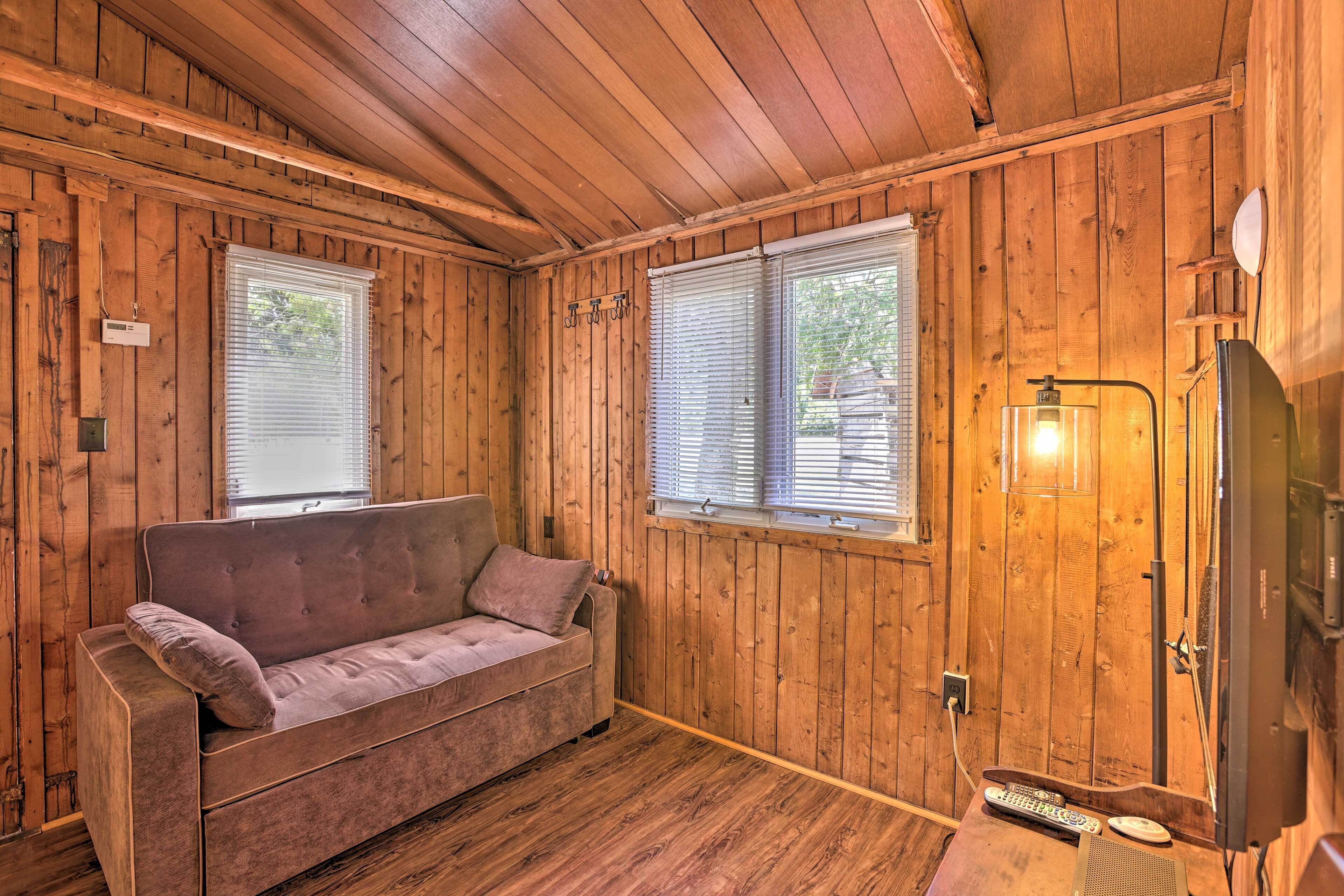 Ein Holzblockhaus-Interieur mit einer Couch, einem Fernseher und einem Fenster mit Jalousien.