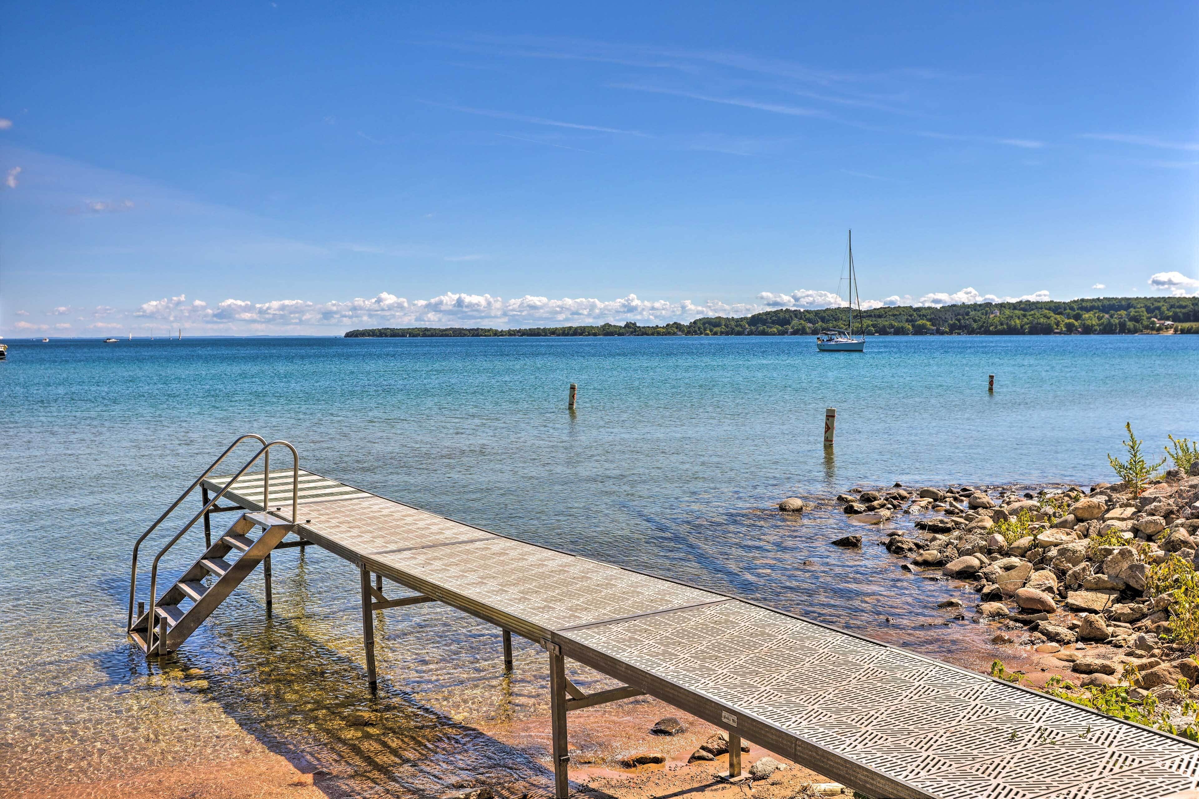 A wooden pier extending into a calm body of water with clear water, surrounded by rocks and vegetation.