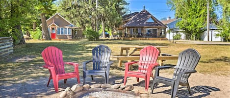Un espace extérieur accueillant, aménagé avec des fauteuils Adirondack et un foyer, entouré d’un cadre naturel avec des arbres et un chalet en arrière-plan.