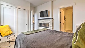 A bedroom with a bed, a television mounted above a fireplace, and a door leading to another room. - Grand Lake Condo w/ Balcony & Mountain Views (Grand Lake)