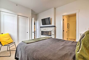 A bedroom with a bed, a television mounted above a fireplace, and a door leading to another room.