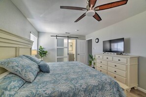 A bedroom with a bed, a ceiling fan, a dresser, a television, and a plant.