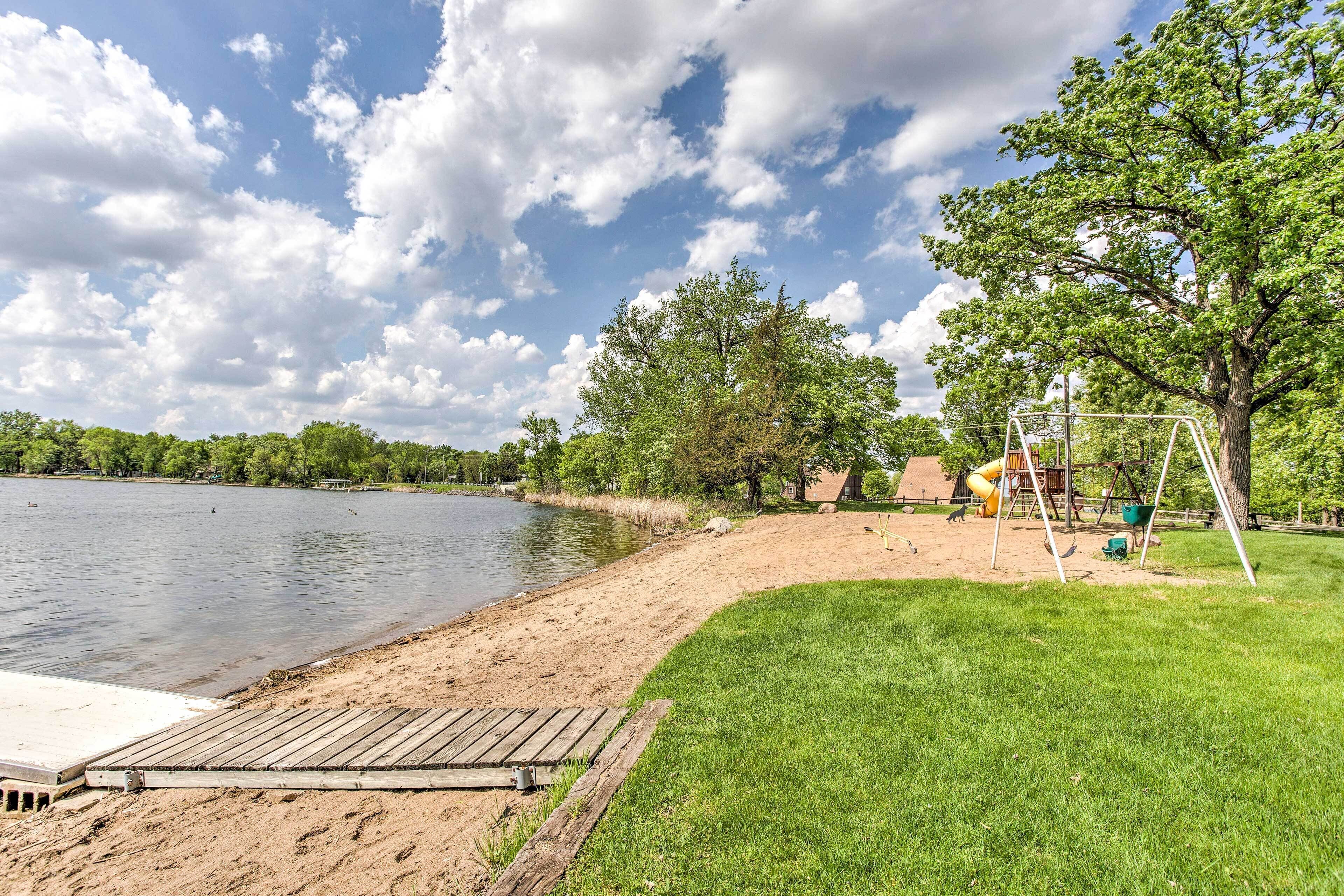A lakeside park with a wooden dock, grassy areas, and a playground.