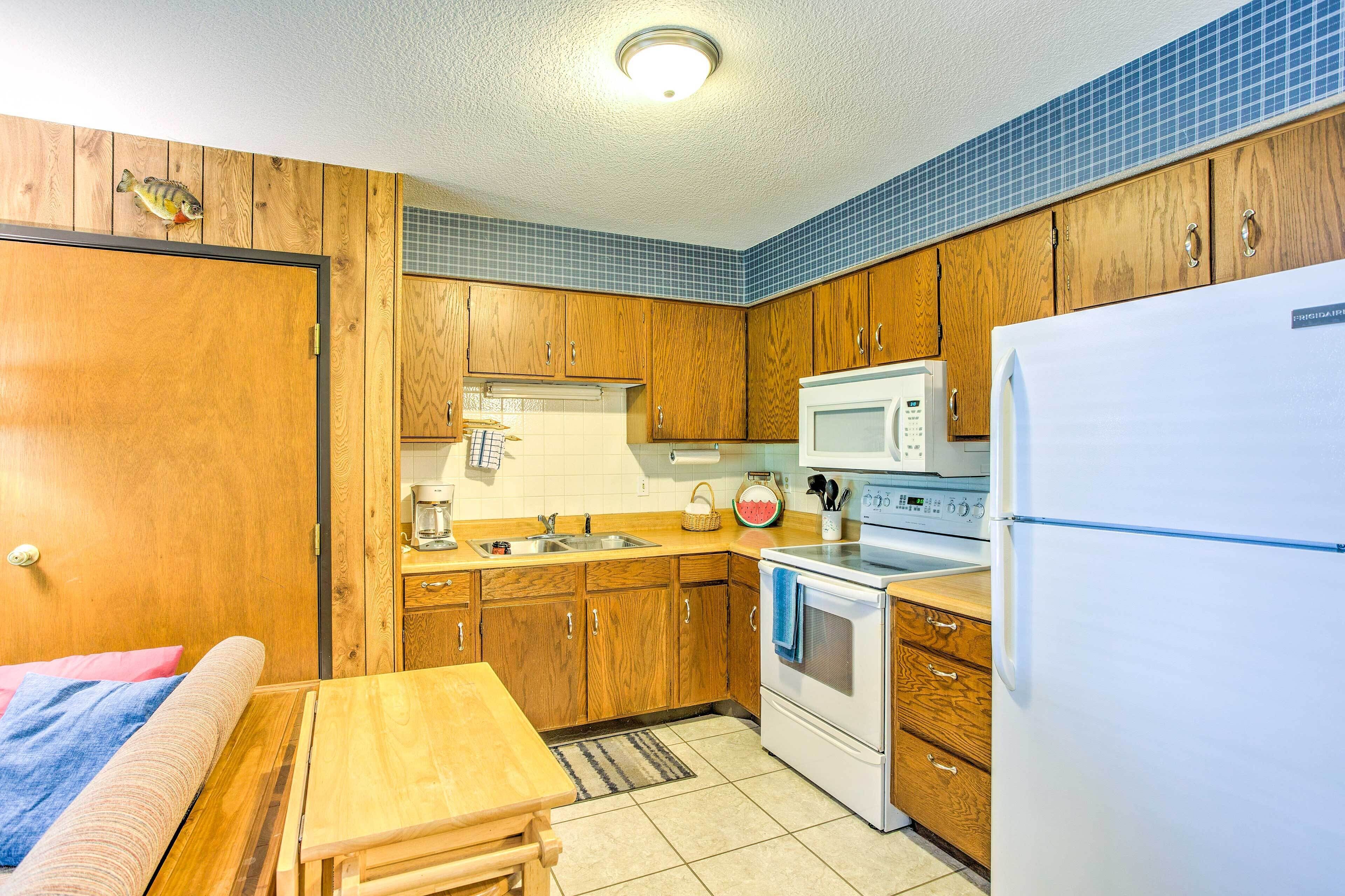 A compact kitchen with wooden cabinets, a microwave, a refrigerator, and a small dining area.