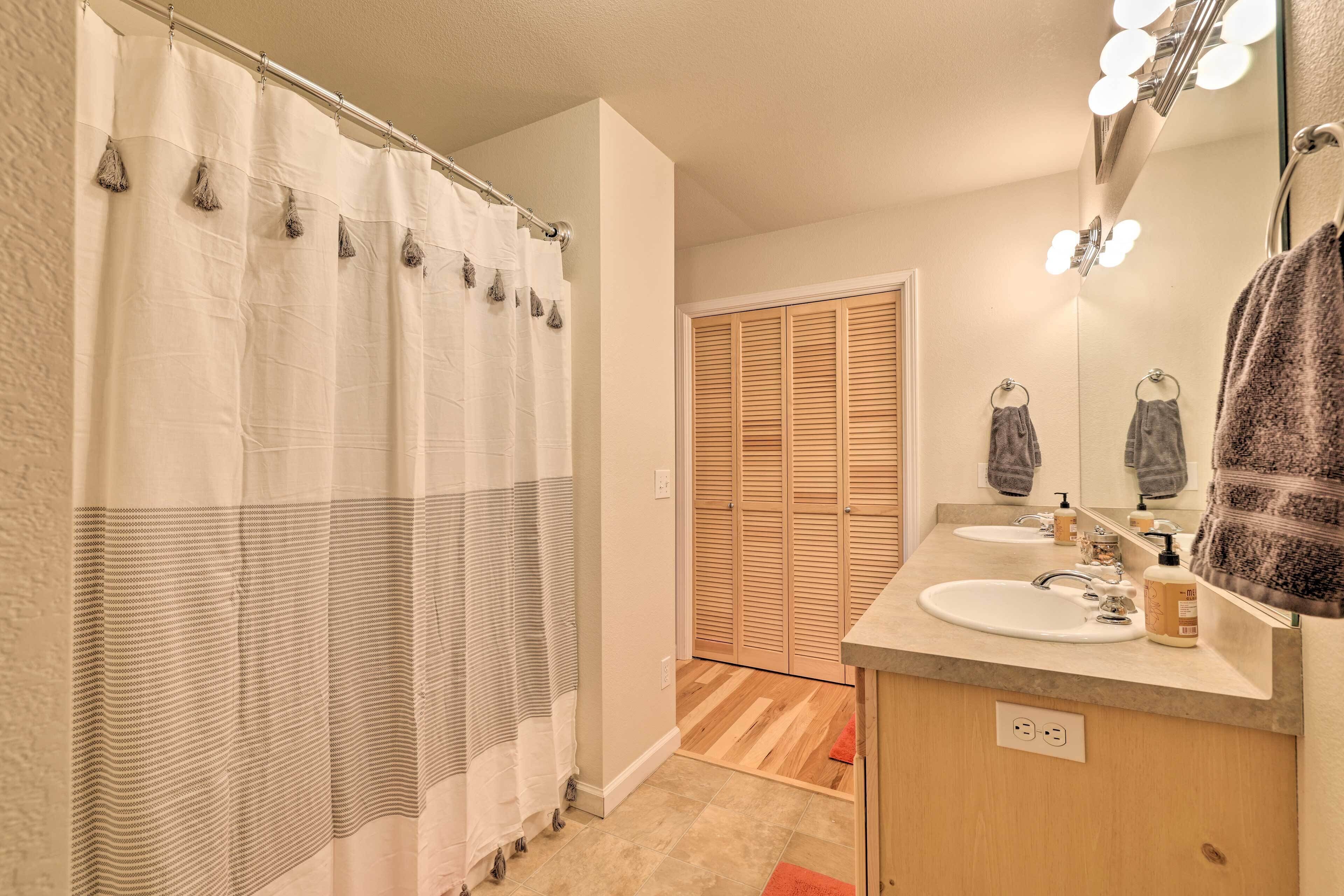 Une salle de bain avec un rideau de douche, un plancher en bois, deux lavabos, un miroir avec éclairage et un porte-serviettes.