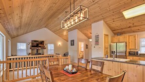A spacious dining area with wooden furniture and a central island, a kitchen with wooden cabinets and modern appliances, and a high ceiling with exposed beams. - Cold Springs Mountain Cabin: Hot Tub & Generator (Long Barn)