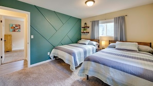 Un dormitorio con dos camas, una pared de acento color turquesa, una ventana con cortinas y una mesita de noche con lámpara.