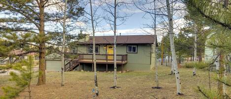 A house with a deck, surrounded by trees and a grassy yard.