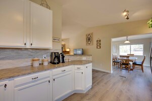 Cocina con armarios blancos, encimera de mármol y una zona de café.