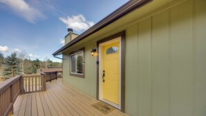 Una terraza de madera que conduce a una puerta amarilla con un ventanal arriba.