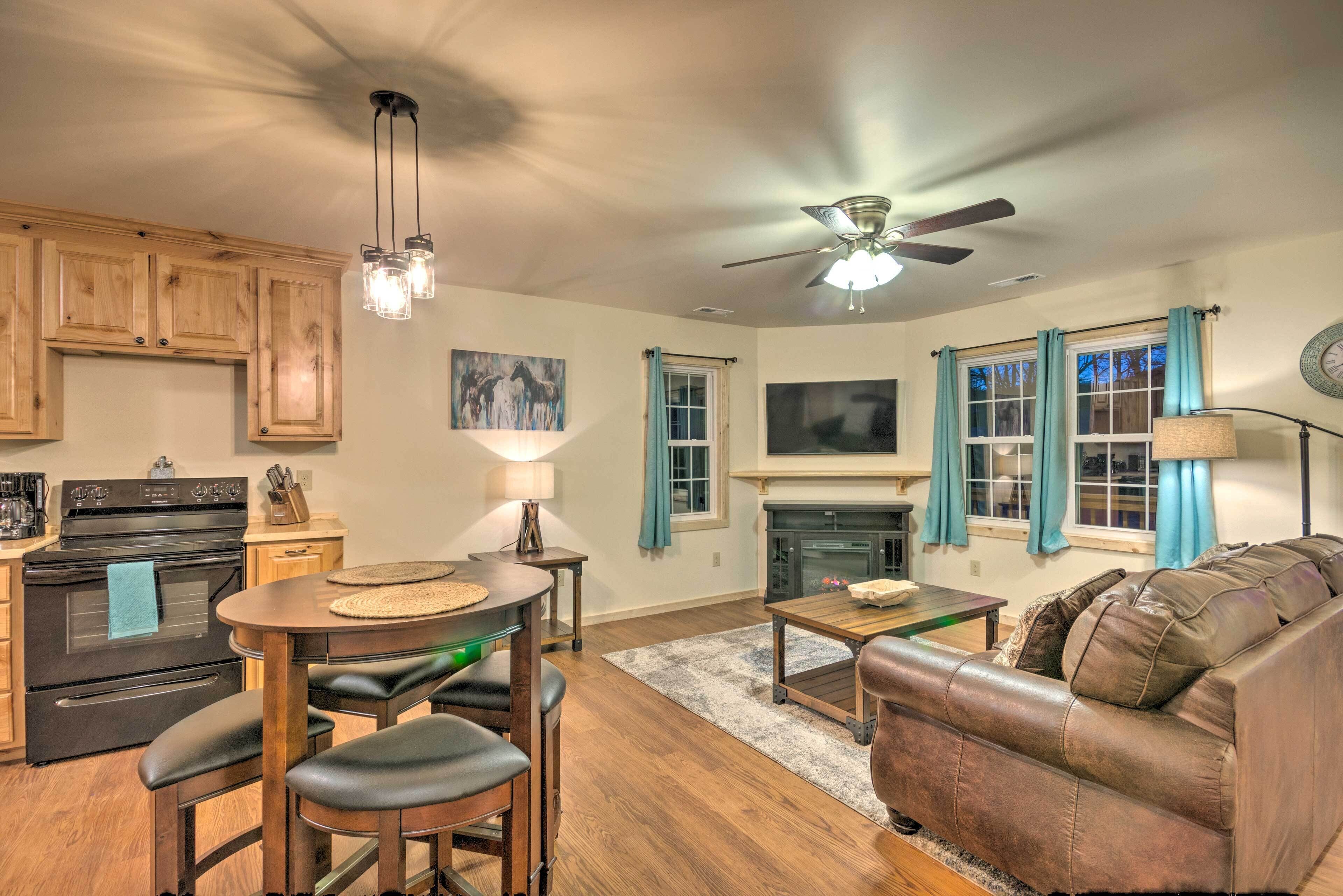 A modern kitchen with wooden cabinets, a black stove, and a dining area with a round table and bar stools.