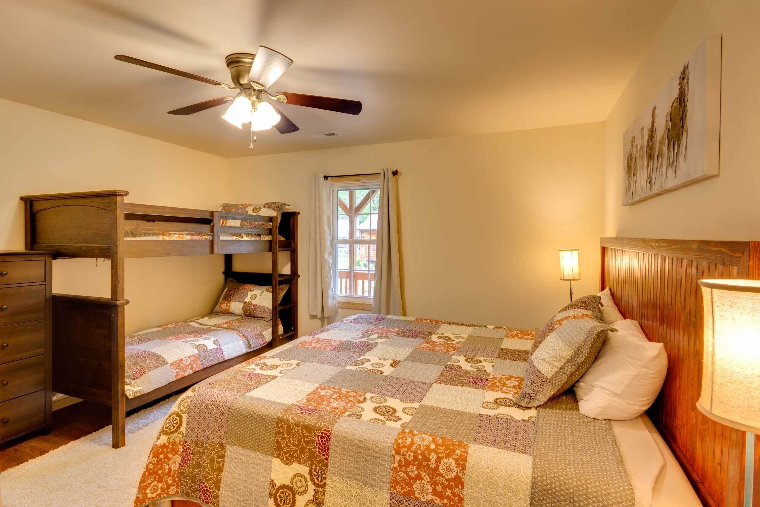 A bedroom with a bunk bed, a single bed, a ceiling fan, a window with curtains, and a painting on the wall.