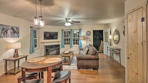 A cozy living room with a fireplace, a ceiling fan, and a dining area with a wooden table and chairs. - Fire Pit: Cozy Bryson City Cabin on Tuck River (Bryson City)
