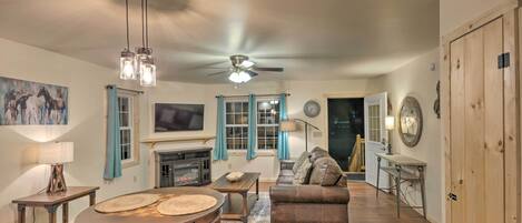 A cozy living room with a fireplace, a ceiling fan, and a dining area with a wooden table and chairs.