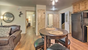 A modern kitchen with a black refrigerator, wooden cabinets, and a dining area with a round table and chairs. - Fire Pit: Cozy Bryson City Cabin on Tuck River (Bryson City)