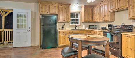 A kitchen with wooden cabinets, a black refrigerator, a microwave, an oven, and a dining area with stools.