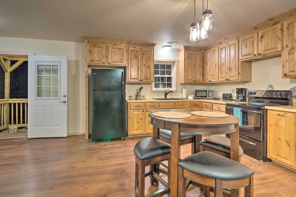A kitchen with wooden cabinets, a black refrigerator, a microwave, a stove, and a dining area with stools.