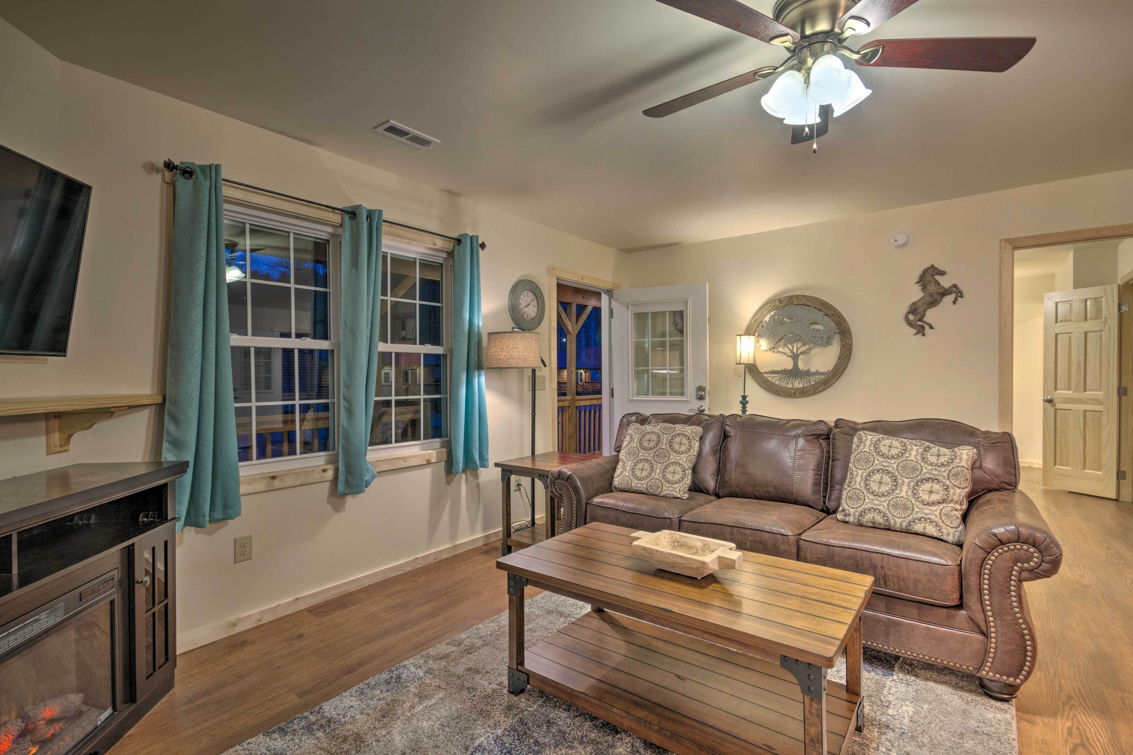 A living room with a brown leather sofa, a wooden coffee table, a ceiling fan, and a fireplace.