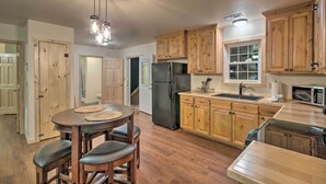 A kitchen with wooden cabinets, a black refrigerator, a microwave, and a dining area with a round table and stools. - Fire Pit: Cozy Bryson City Cabin on Tuck River (Bryson City)