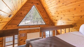 L’intérieur d’une cabane en bois, avec une fenêtre triangulaire, un lit et un panneau indiquant la sortie.