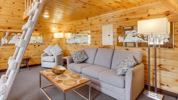 L’intérieur d’un chalet confortable, avec des murs en rondins, un canapé, une petite table et une échelle.