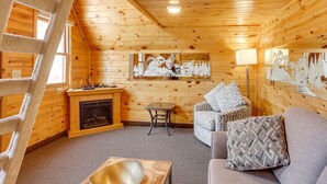 L’intérieur d’un chalet confortable, avec une cheminée, un canapé, une petite table et une échelle.
