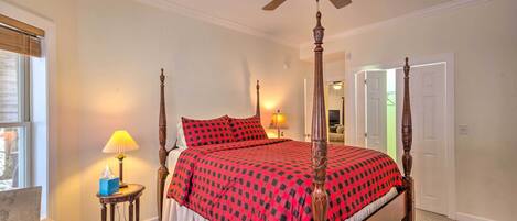 A four-poster bed with a red and black checkered bedspread, a wooden nightstand with a lamp, and a ceiling fan.