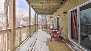 Une terrasse en bois dotée d’un porche couvert, d’une porte-fenêtre coulissante et de deux fauteuils Adirondack.
