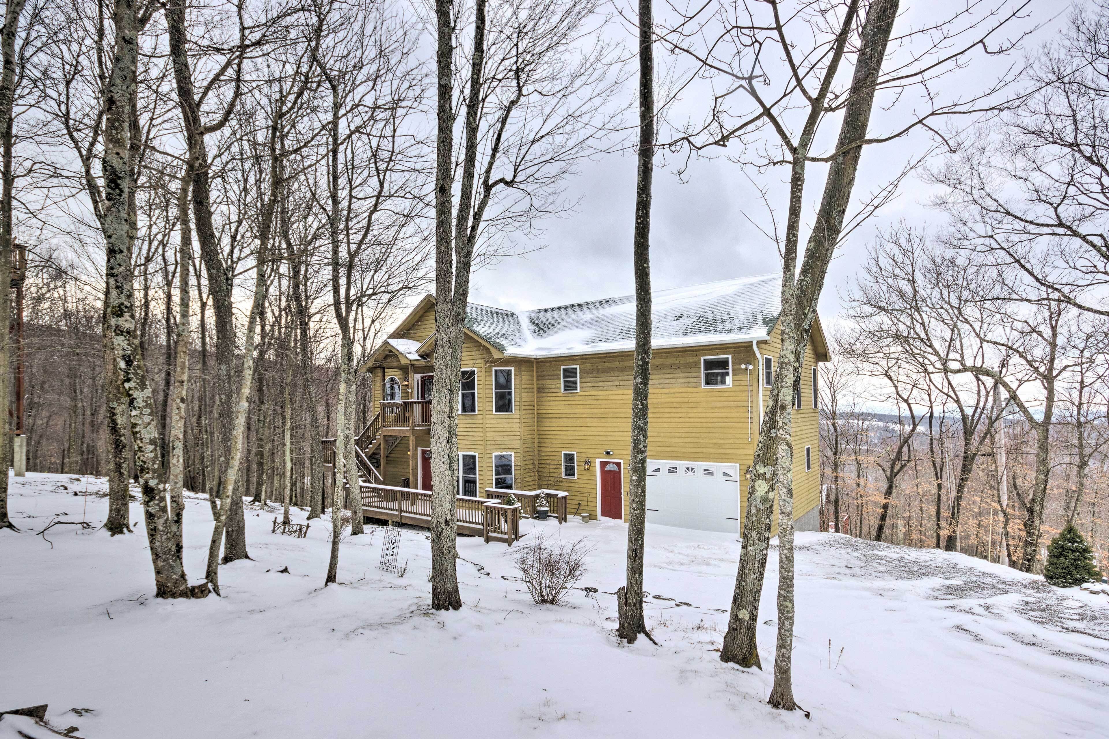 A two-story yellow house with a covered porch, surrounded by snow-covered ground and leafless trees.