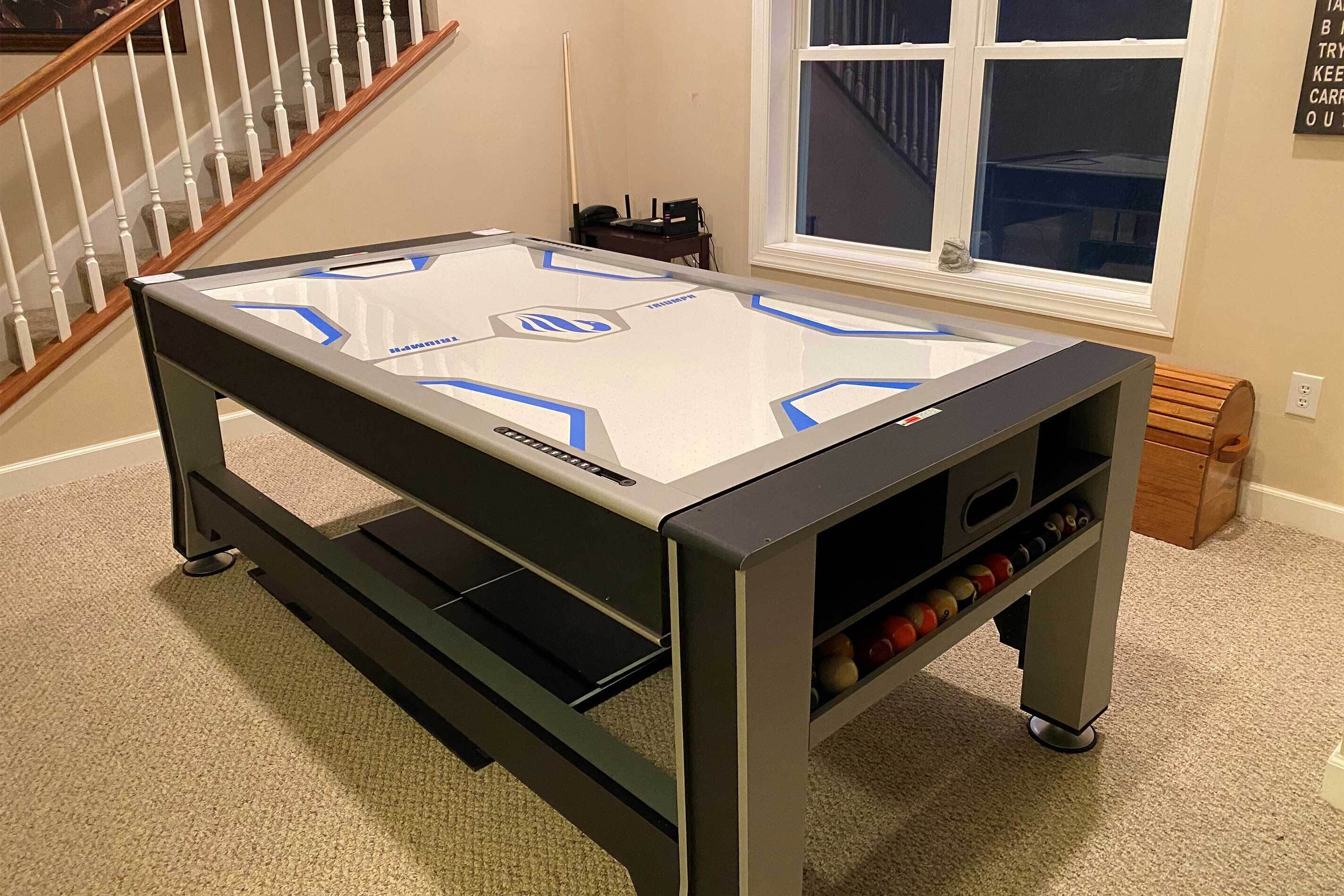 A pool table with a black and white table, a shelf with billiard balls, and a window with a view of a staircase.