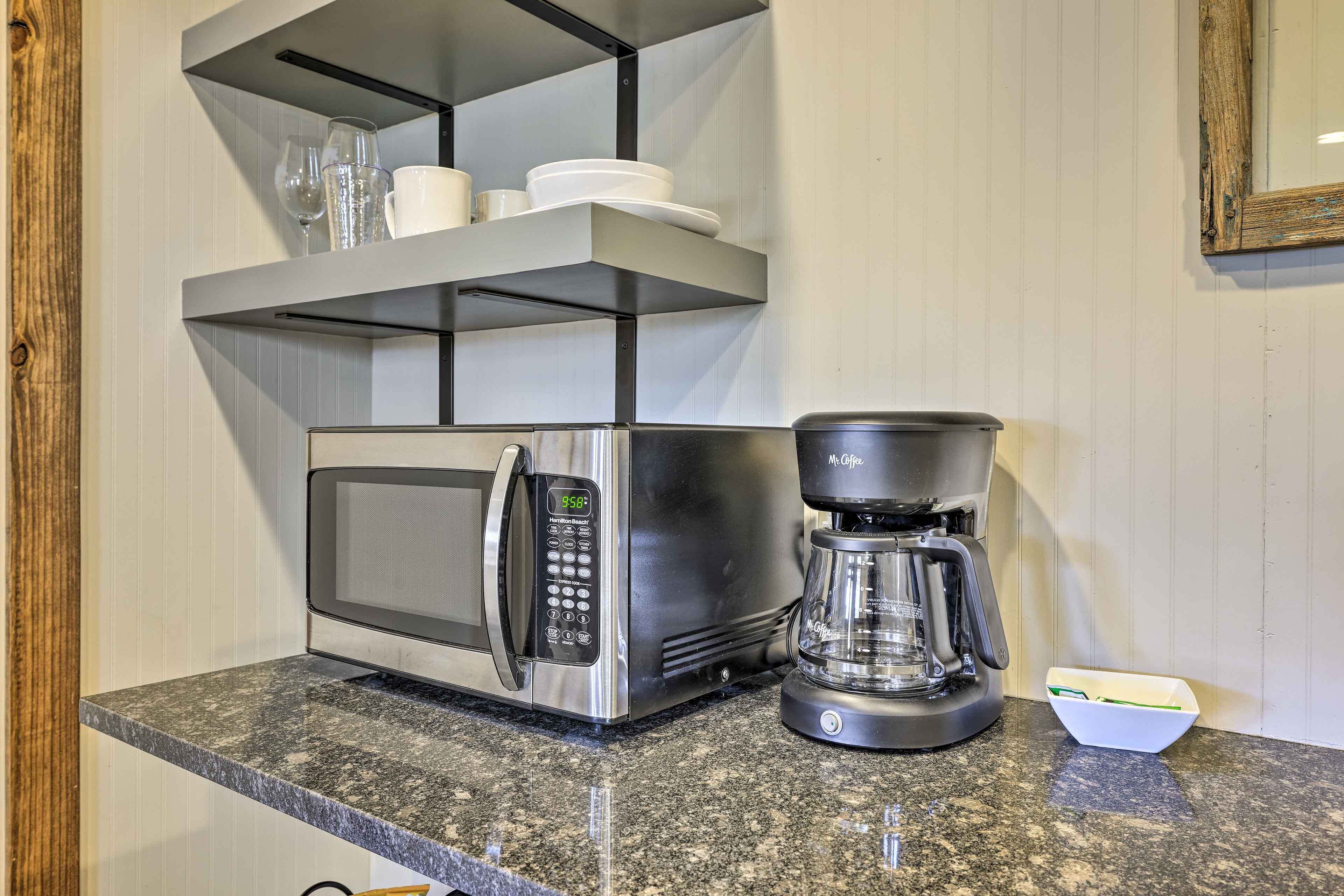 A kitchen with a built-in microwave and coffee maker, a shelf with cups and glasses, and a granite countertop.