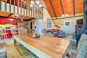 Amplio espacio tipo loft con una gran mesa de comedor de madera, una cocina con armarios rojos y un techo alto con vigas a la vista.