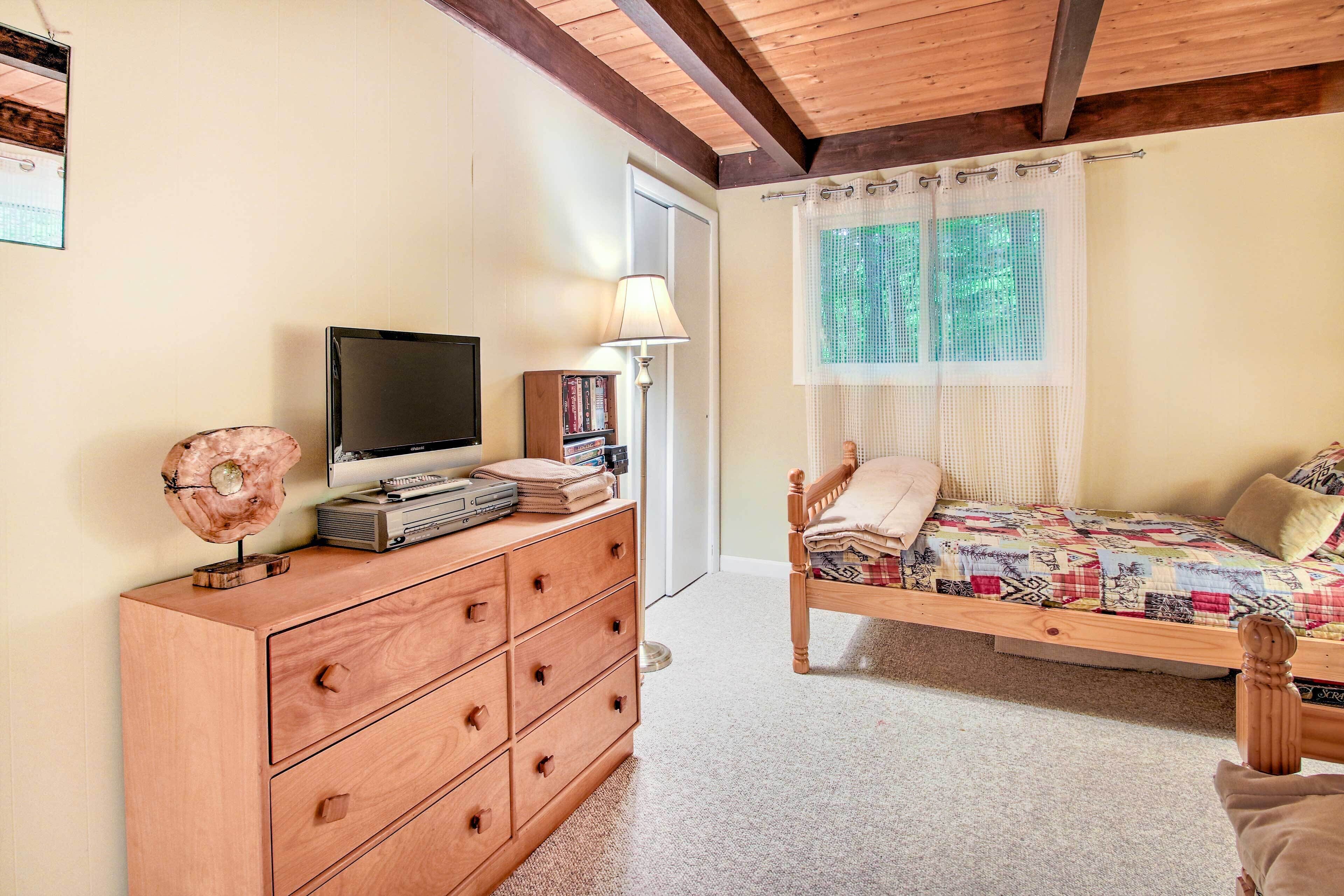 A bedroom with a wooden dresser, a bed with a quilt, a television, and a window with curtains.